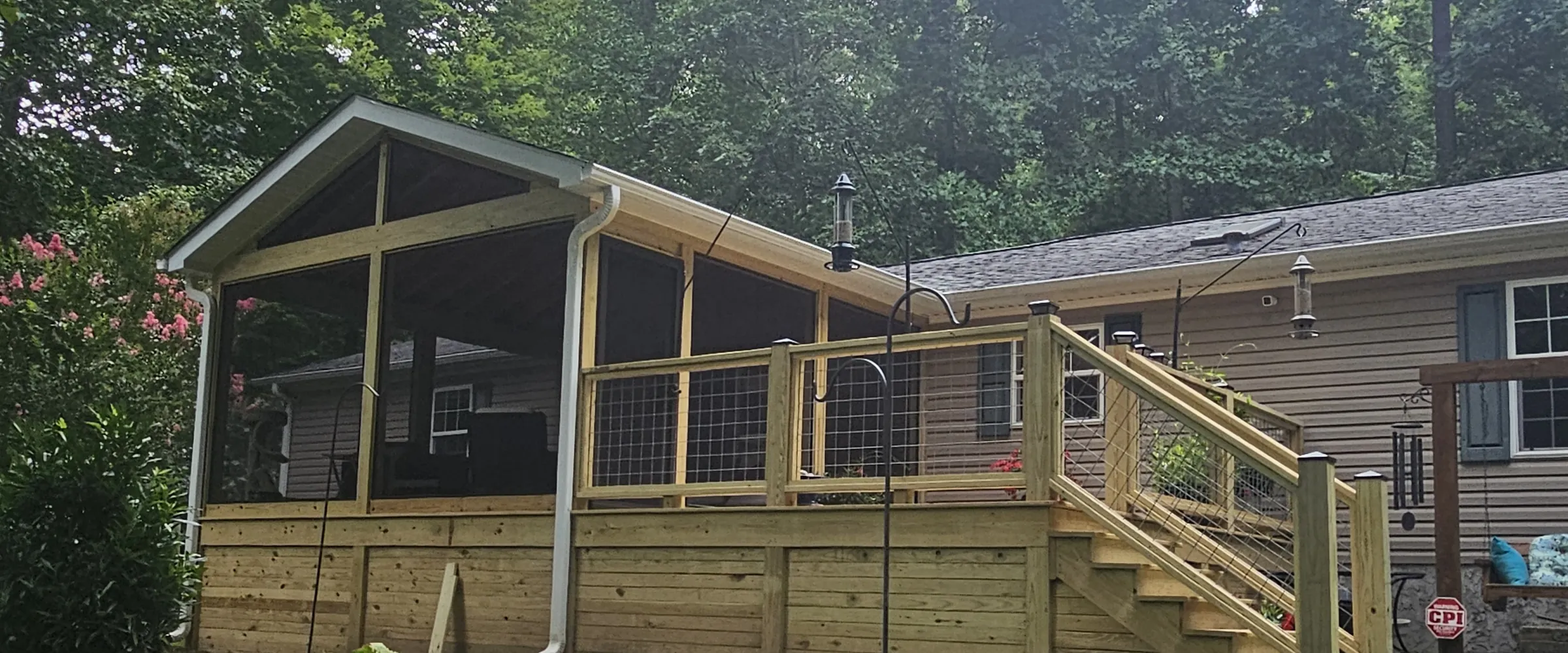 Screened porch and deck built by Lozica Builders, with cable railing and planted borders